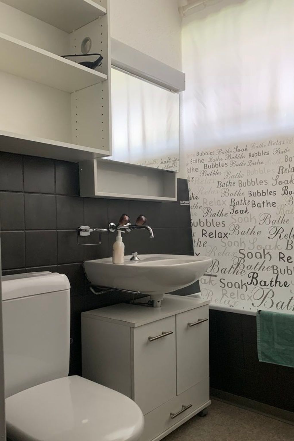 A bathroom with a white sink, a toilet, and a cabinet. There is a towel hanging on the wall.