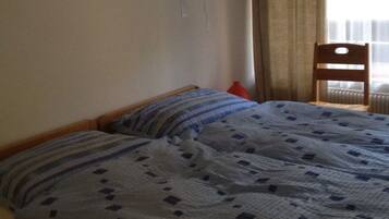 A bedroom with two beds, a wooden chair, and a radiator.