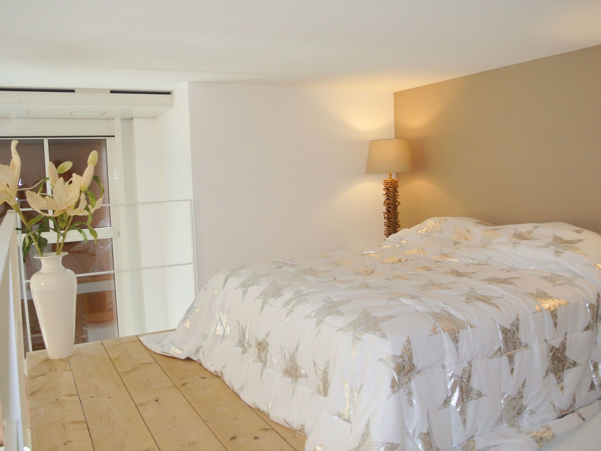 Une chambre à coucher avec un lit, une table de chevet, une lampe et un vase de fleurs.
