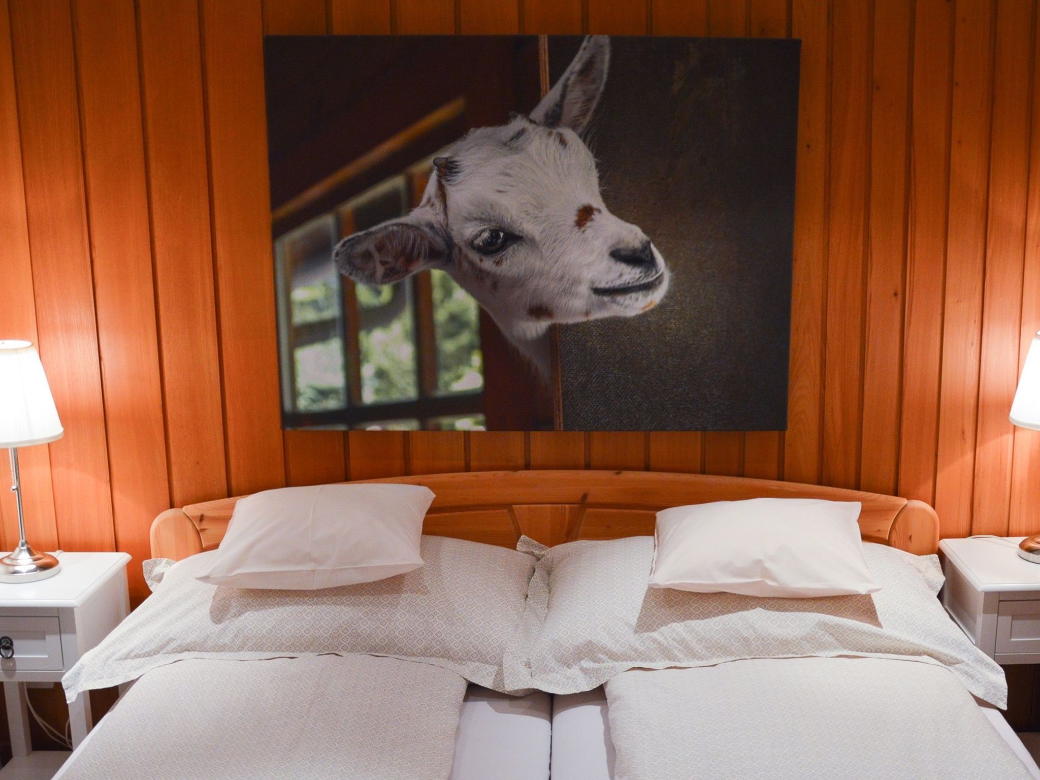 A hotel room with a wooden headboard, a large bed with white linens, and a framed picture of a calf on the wall.