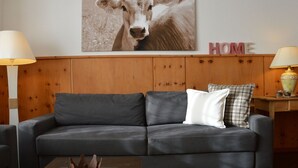 A living room with a grey sofa, a decorative crown on a table, and a wall-mounted picture of a cow. - Rothmund, (Bad Ragaz), by Interhome (Bad Ragaz)