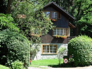 A two-story wooden house with large windows and a stone foundation, surrounded by lush greenery. - Rothmund, (Bad Ragaz), by Interhome (Bad Ragaz)