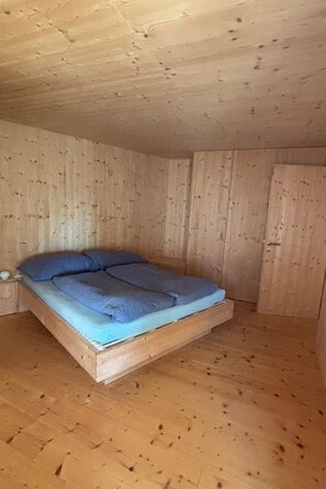 A room with a wooden floor and walls, a bed with blue bedding, and a wooden door. - Casa Mia Pardiel, (Bad Ragaz), by Interhome (Bad Ragaz)