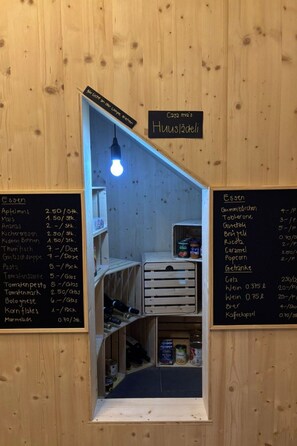 A small, cozy kitchenette with wooden walls and a hanging light bulb. There are two chalkboards listing food items and prices.