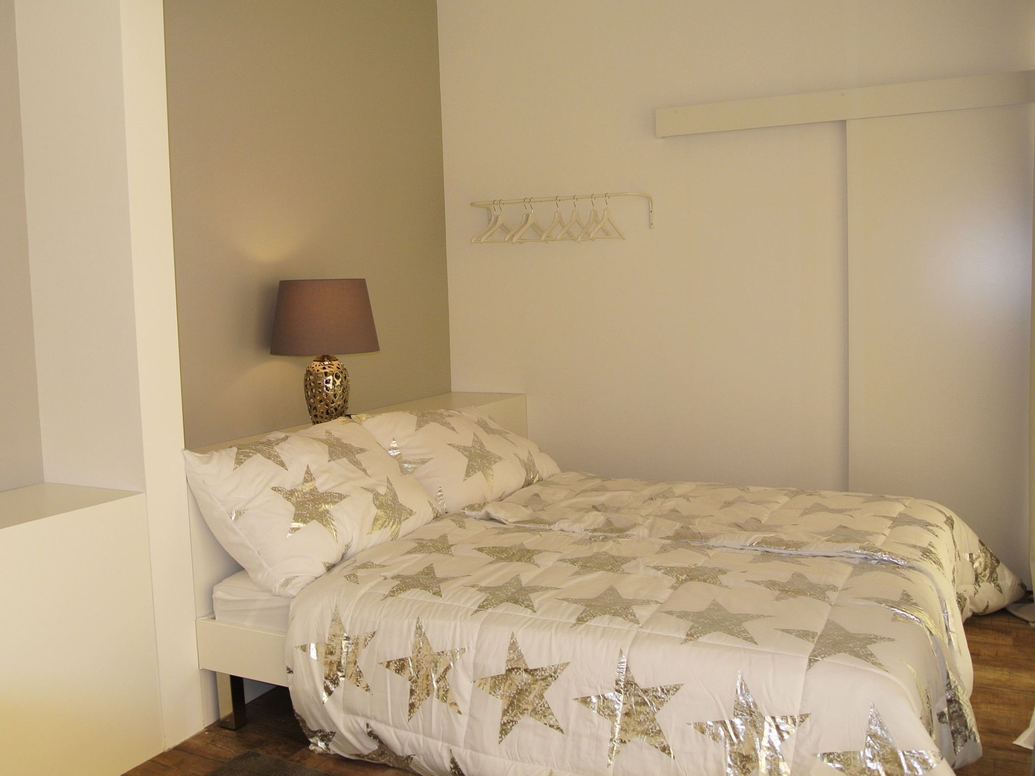 A bedroom with a bed, a nightstand, a lamp, and a wall-mounted shelf.
