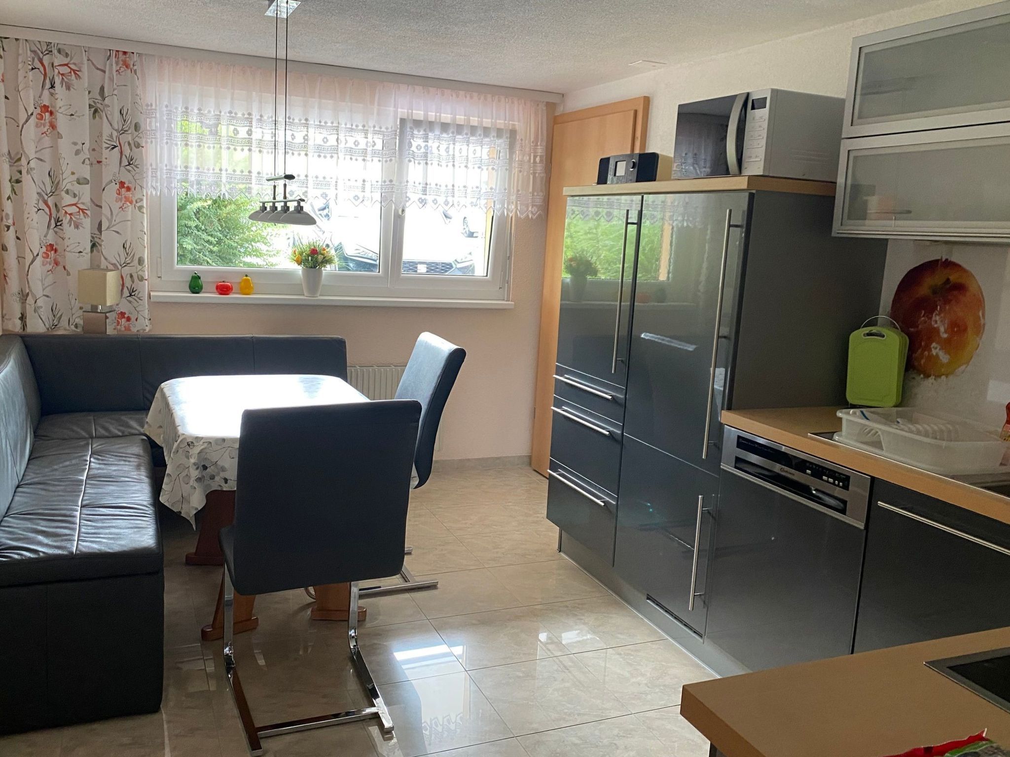 A compact kitchen with a dining area, a sofa, and a window with curtains.