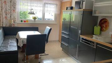 A compact kitchen with a dining area, a sofa, and a window with curtains.