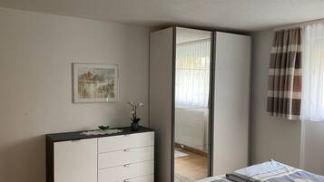 A bedroom with a bed, a dresser, a mirror, a window with curtains, and a wall-mounted picture.