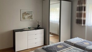 Un dormitorio con cama, cómoda, espejo, ventana con cortinas y un cuadro en la pared.