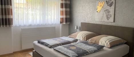 Un dormitorio con cama, cortinas, un radiador, una lámpara de pared y un cuadro enmarcado.
