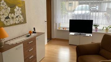 A living room with a sofa, a TV on a stand, a painting on the wall, and a window with blinds.