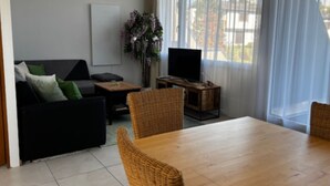Ein Wohnzimmer mit Sofa, Fernseher, Esstisch und Stühlen.