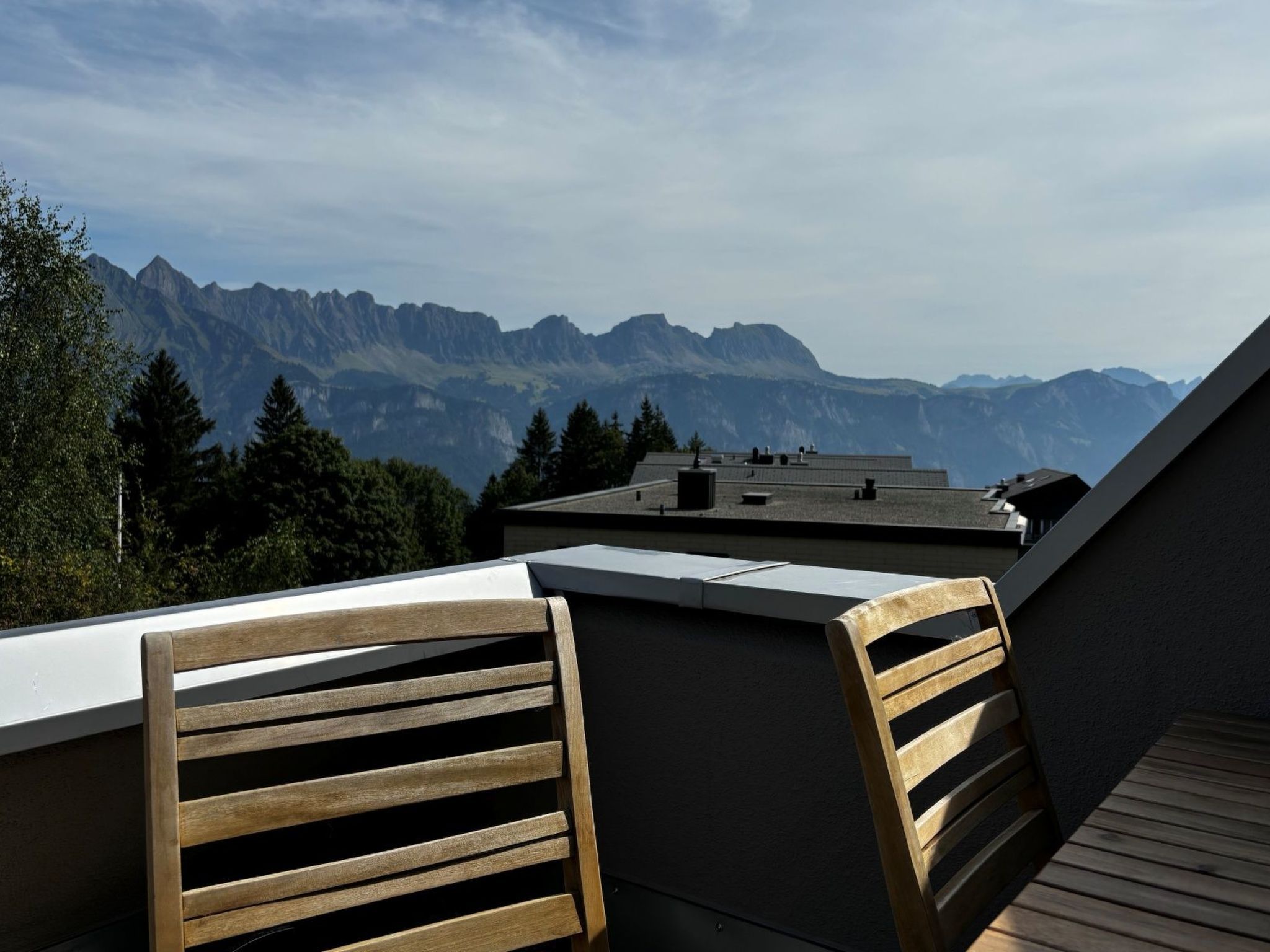 A balcony with wooden chairs, a table, and a view of mountains.