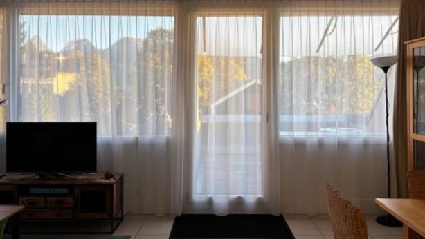 Ein Zimmer mit einem großen Fenster, einem Fernseher auf einem Holzboden, einem Esstisch und einem Stuhl.