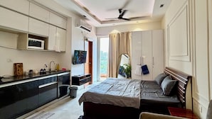 Ein modernes Hotelzimmer mit Küchenzeile, einem Bett mit Kopfteil, einer Sitzecke mit Tisch und einem Deckenventilator.