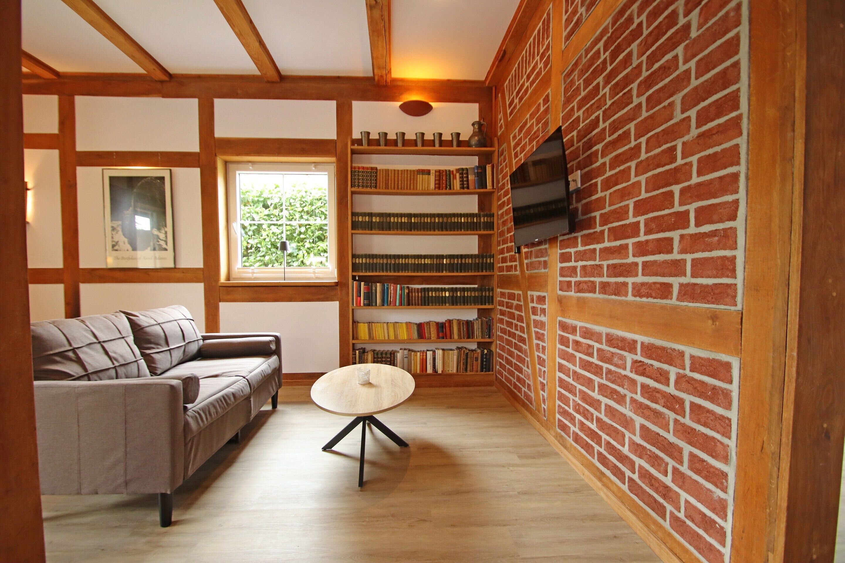 A room with a sofa, a round table, a bookshelf, and a brick wall.