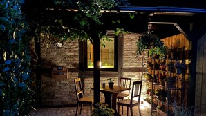 Un patio al aire libre con pared de ladrillo, sillas de madera, una mesa y plantas en macetas.