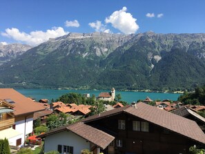 Un paysage montagneux avec un lac, des maisons aux toits rouges et le clocher d’une église.
