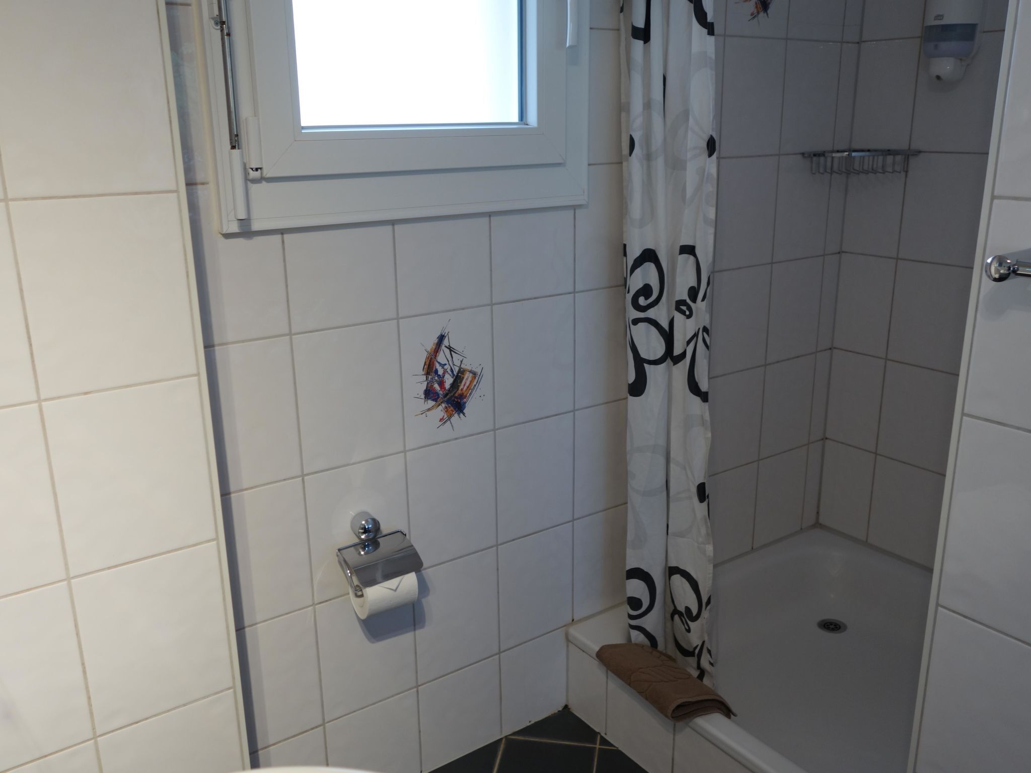 A bathroom with a shower, toilet, and a window.