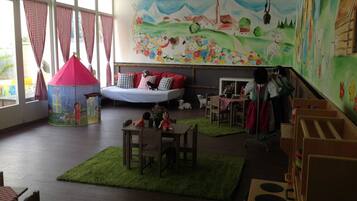 Un cuarto de juegos acogedor para niños con una cama, corralito y un mural en la pared.
