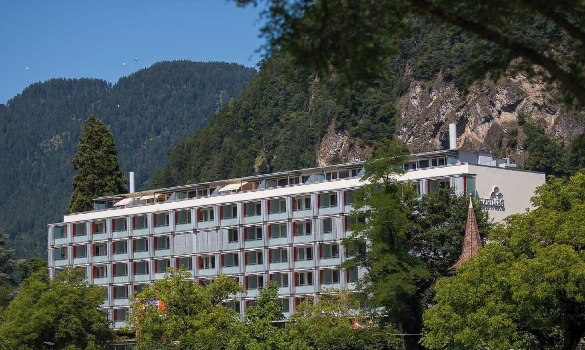 A multi-story hotel with a modern architectural design, situated in a mountainous area with trees in the foreground.