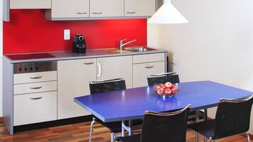 Una cocina compacta con salpicadero rojo, un lavamanos, una cafetera y un comedor con una mesa azul y cuatro sillas.