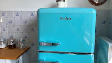 Ein türkisfarbenes Amica-Kühlschrank in einer Küche mit gefliestem Fliesenspiegel, einer Holz Arbeitsplatte und einem kleinen Hocker.