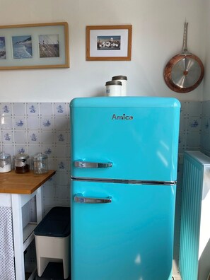 A turquoise Amica refrigerator in a kitchen with tiled backsplash, a wooden countertop, and a small stool.