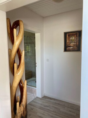A hallway with a wooden sculpture, a glass shower door, and a framed picture on the wall. - Cozy vacation rental in a quiet location in Molfsee, near the Baltic Sea (Molfsee)
