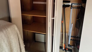 Une pièce avec un lit en mezzanine, une armoire en bois et un petit placard avec un miroir et un balai.
