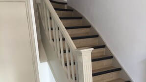 Un escalier avec des marches en bois et des contremarches noires, menant à l’étage supérieur.