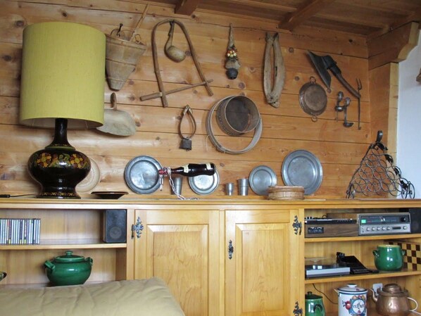 Ein rustikaler Holzraum mit einem Bett, Regalen mit Küchenutensilien und einer Wandlampe.
