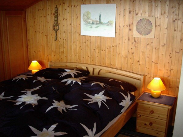 A wooden-paneled room with a bed, two bedside lamps, a nightstand, and wall art. - Uf dr Braue Appartement/Fewo 6-Bettwohnung by Interhome (Beatenberg)