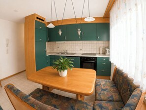A compact kitchen with green cabinets, a wooden dining table, and a patterned sofa. - Residenz Darianne Leukerbad # 4-bed apartment, Dusche und Bad, WC by Interhome (Leukerbad)