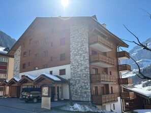 A multi-story hotel with stone and wooden exterior, balconies, and a parking area. - Residenz Darianne Leukerbad # 4-bed apartment, Dusche und Bad, WC by Interhome (Leukerbad)
