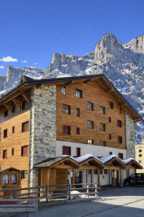 A multi-story hotel with stone and wooden exterior, multiple windows, and a view of snow-capped mountains. - Residenz Darianne Leukerbad # 4-bed apartment, Dusche und Bad, WC by Interhome (Leukerbad)