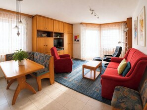 A living room with a sofa, armchairs, a coffee table, a TV, and wooden cabinets. - Residenz Darianne Leukerbad # 4-bed apartment, Dusche und Bad, WC by Interhome (Leukerbad)