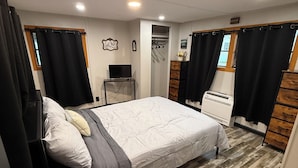 A bedroom with a bed, a dresser, a desk with a computer, a wardrobe, and a window with curtains.
