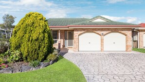 A residential house with a brick exterior, two garage doors, a well-maintained lawn, and a large coniferous tree. - Yannarie: 3  BR, 1.5  BA House in South West Rocks, Sleeps 7 (South West Rocks)