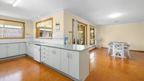 A kitchen with white cabinets, a countertop, a sink, and a dining area with a table and chairs. - Yannarie: 3  BR, 1.5  BA House in South West Rocks, Sleeps 7 (South West Rocks)