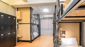 Ein kleines Hotelzimmer mit Etagenbetten, einem Schrank, einem Nachttisch und einem kleinen Regal.