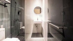 Ein modernes Badezimmer mit einer Duschkabine aus Glas, einem weißen Waschbecken und einem runden Spiegel.