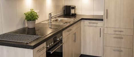 A modern kitchen with light wood cabinetry, a stainless steel sink, a built-in oven, and a coffee maker.