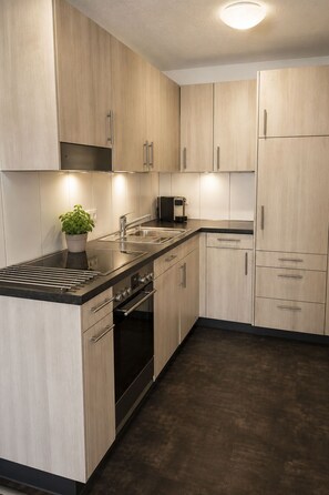 Eine moderne Küche mit hellen Holzschränken, einer Edelstahlspüle, einem Backofen und einer Kaffeemaschine.