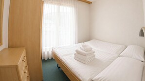 Ett hotellrum med en säng, en garderob i trä, ett fönster med tunna gardiner och en taklampa.
