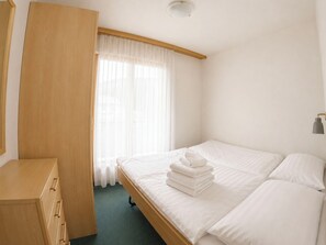 Ein Hotelzimmer mit einem Bett, einem Holzschrank, einem Fenster mit durchsichtigen Vorhängen und einer Deckenleuchte.