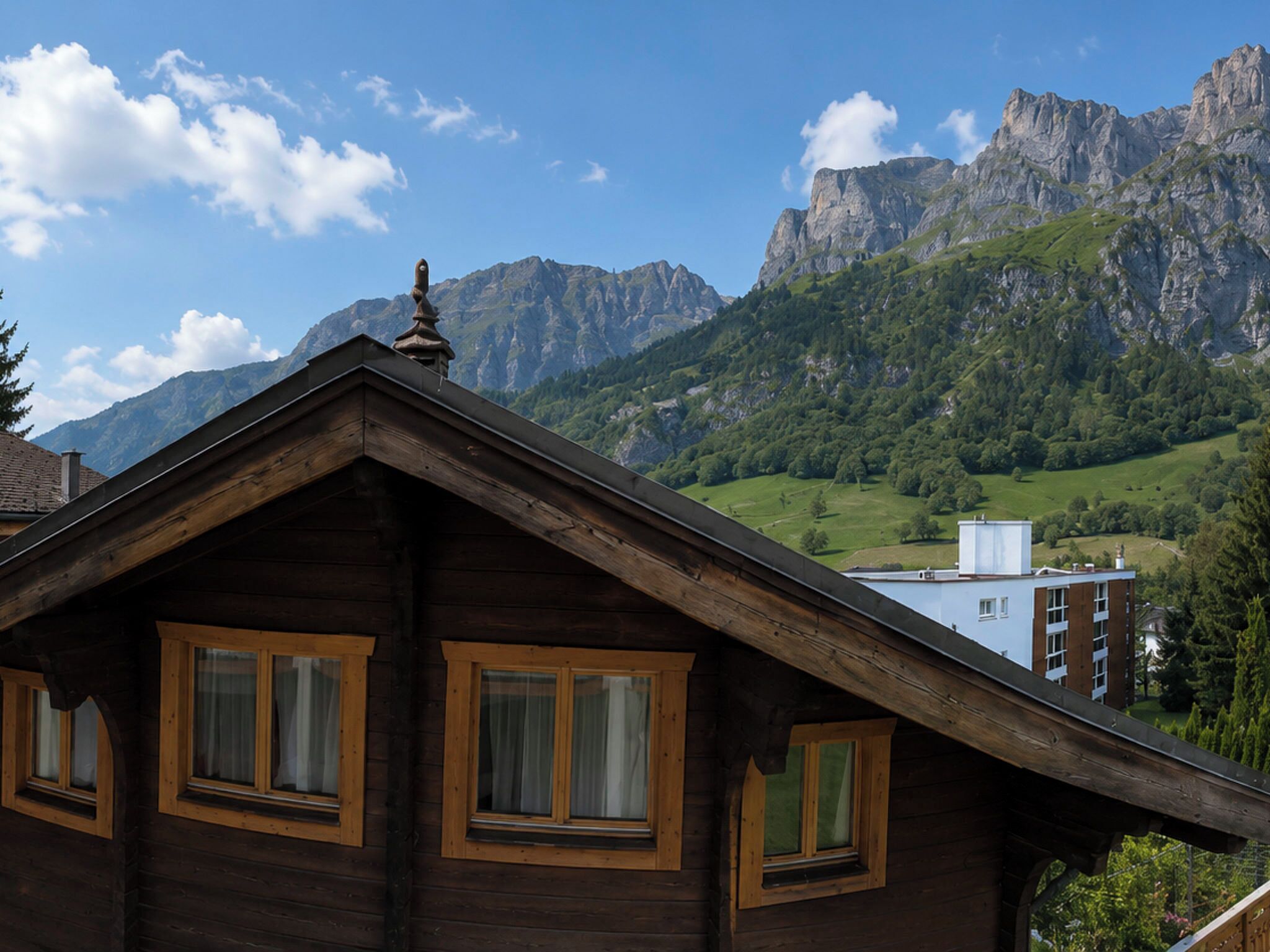 Un chalet en bois doté d’un toit en pente, de nombreuses fenêtres et offrant une vue sur une chaîne de montagnes en arrière-plan.