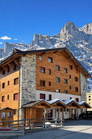 A multi-story hotel with stone and wooden exterior, multiple windows, and a view of snow-capped mountains. - Residenz Darianne Leukerbad # 5-bed apartment, Dusche und Bad, WC by Interhome (Leukerbad)
