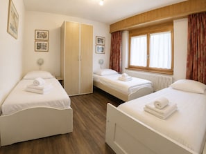 A hotel room with two single beds, a wardrobe, a window with curtains, and framed pictures on the wall. - Residenz Darianne Leukerbad # 5-bed apartment, Dusche und Bad, WC by Interhome (Leukerbad)