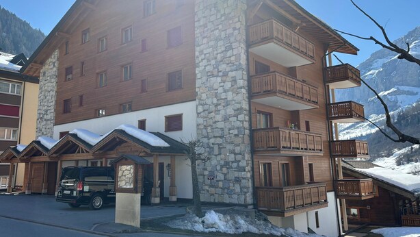 A multi-story hotel with stone and wooden exterior, balconies, and a parking area. - Residenz Darianne Leukerbad # 5-bed apartment, Dusche und Bad, WC by Interhome (Leukerbad)